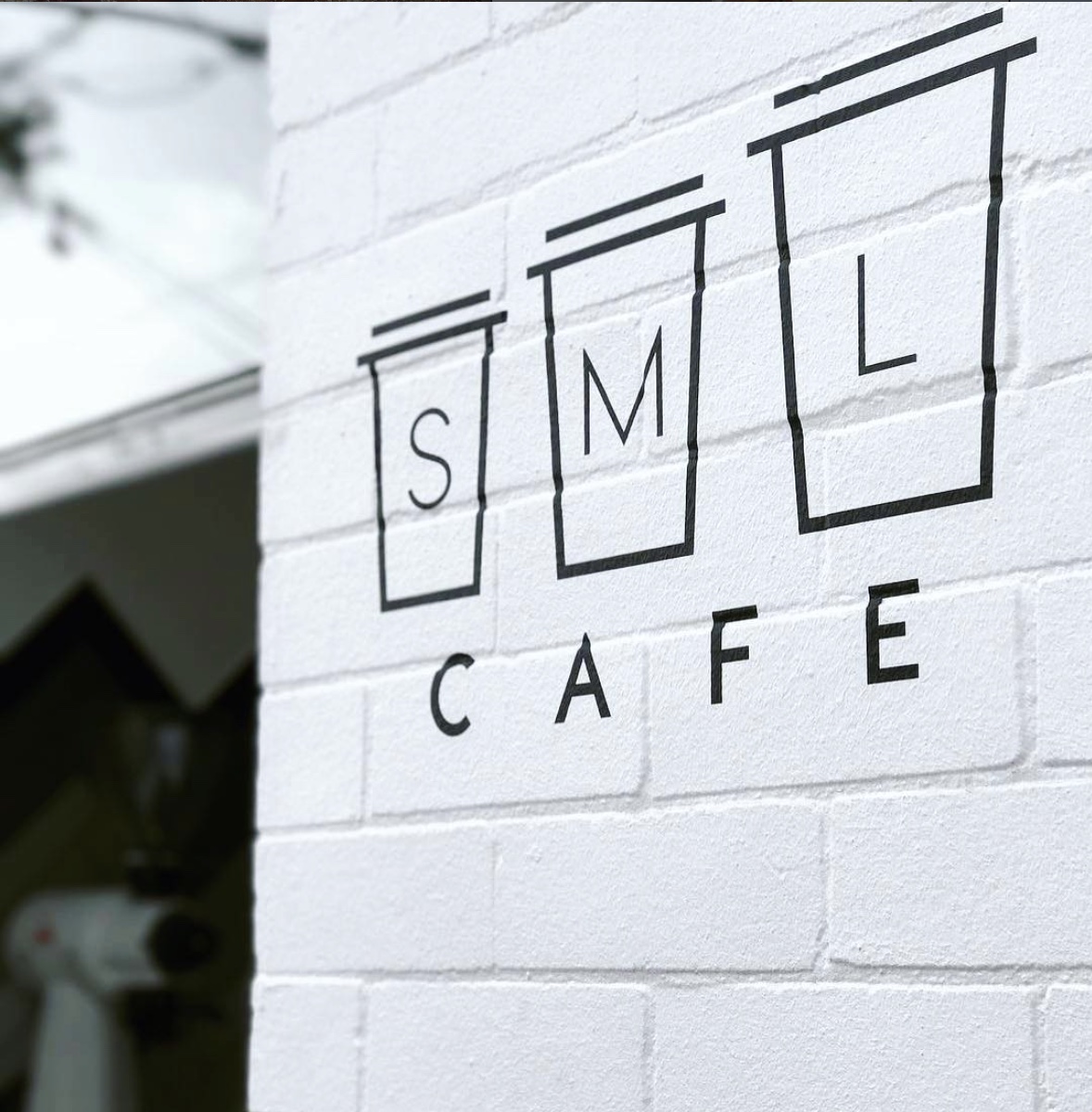 SML Cafe logo painted on a white brick wall